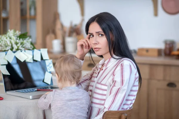 Young mom holding daughter, interfering with her work — Stockfoto