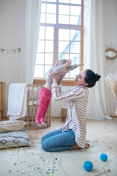 Young mom sitting on the floor and lifting her daughter — Stockfoto