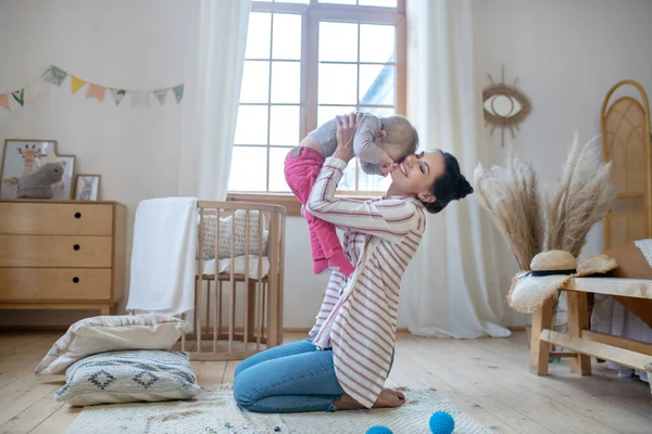 Young mom sitting on the floor, lifting her daughter, smiling — Stockfoto
