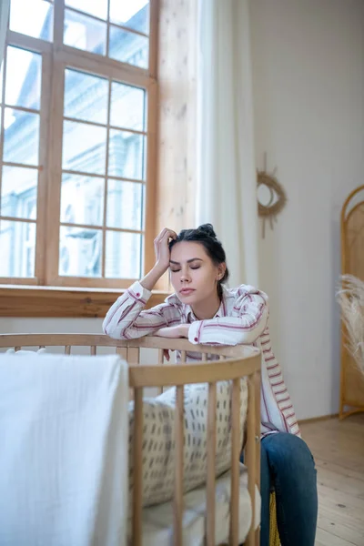 Tired mom sitting at the cot, holding her head — Stockfoto