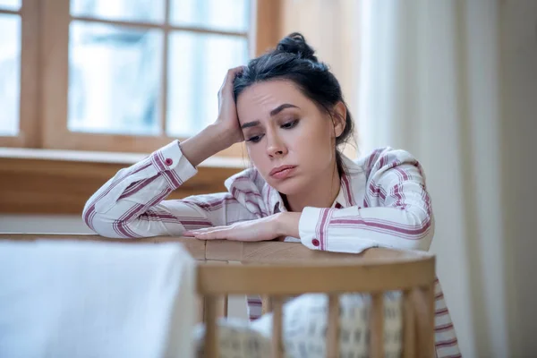 Tired mom sitting with her elbows on the cot, holding her head — Stockfoto