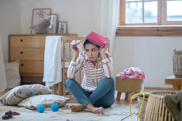 Wanita lelah duduk di lantai dengan buku catatan di kepalanya — Stok Foto