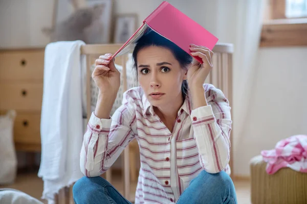 Tired and sad woman sitting on the floor with notebook on her head — Stockfoto