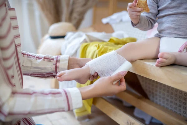 Mãos de mulher aplicando bandagem na perna infantil — Fotografia de Stock