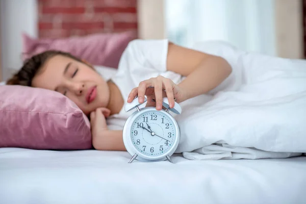 Durmiendo chica adolescente en la cama, la mano en el despertador . — Foto de Stock