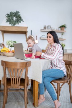 Young mom working at laptop, daughter interfering clipart