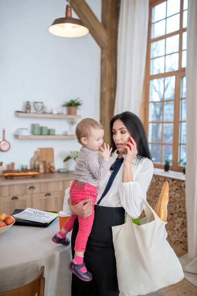 Mom holding daughter and shopping bag, talking on the phone — Stock Photo, Image