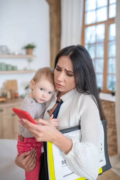 Werkende moeder controleren telefoon, vasthouden van haar baby — Stockfoto