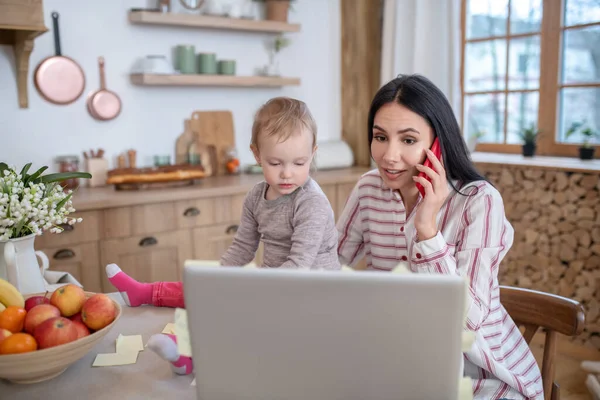 엄마는 딸 과 노트북 컴퓨터 앞에 앉아서, 전화 통화를 하고 있습니다. — 스톡 사진