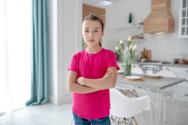 Kollarını kavuşturmuş parlak tişörtlü güzel bir kız.