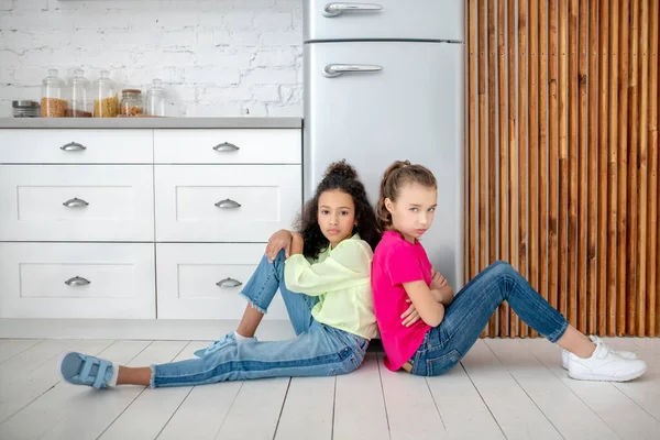 Fille aux cheveux bruns en jeans assis près du réfrigérateur avec son ami — Photo