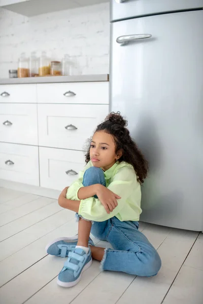 Σκούρα μαλλιά κορίτσι με τζιν κάθεται κοντά στο ψυγείο αισθάνεται πεινασμένοι — Φωτογραφία Αρχείου