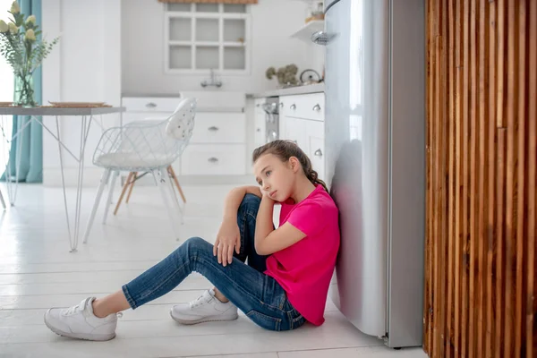 Menina em camiseta brilhante sentado no chão sentindo-se triste — Fotografia de Stock