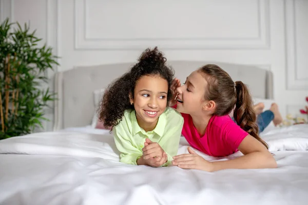 Duas garotas deitadas na cama compartilhando segredos — Fotografia de Stock