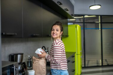 Genç bir kadın mutfak tezgahında duruyor, elinde Asyalı yemek kutusu var.