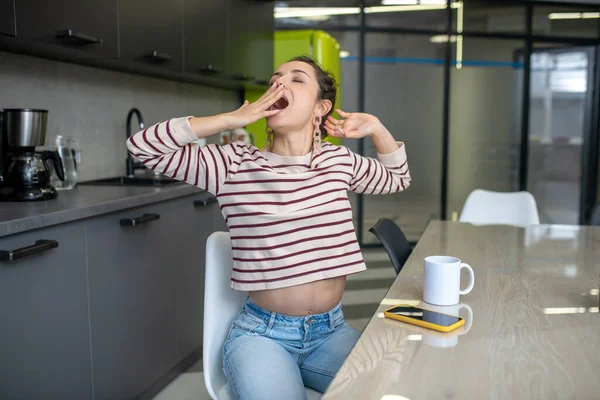 若い女性は台所に座って、ストレッチ、あくびをする — ストック写真