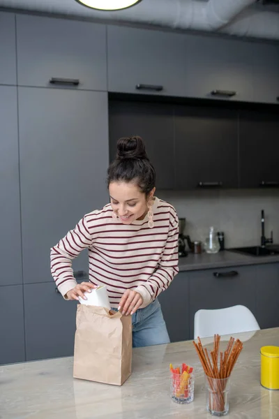 Молодая женщина распаковывает коробку с обедом на кухне — стоковое фото