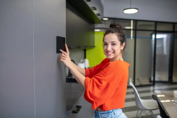 Jovem segurando tablet contra a parede da cozinha, sorrindo — Fotografia de Stock