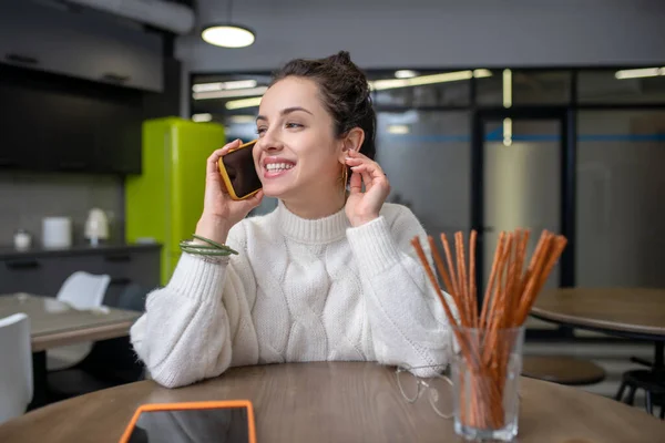 Mladá žena sedí v kuchyni a telefonuje. — Stock fotografie