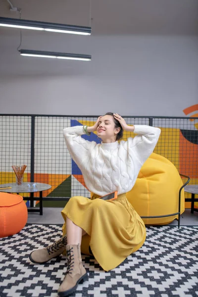 Mujer joven sentada en la silla del bolso, piernas cruzadas, estiramiento — Foto de Stock