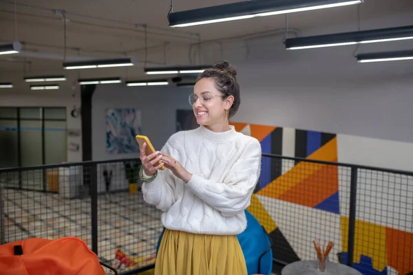 Jovem mulher em óculos, verificando seu telefone, sorrindo — Fotografia de Stock