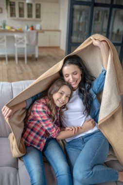 Anne ve kızı ekoseyle kaplı bir kanepede oturuyor.