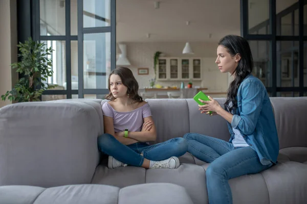 Mom in a jeans jacket talking to her daughter holding a smartphone in her hands