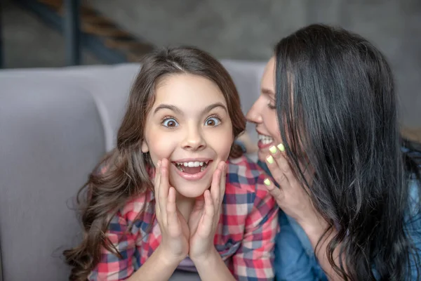 Donkerharige moeder vertelt iets interessants aan haar verbaasde dochter in het oor — Stockfoto