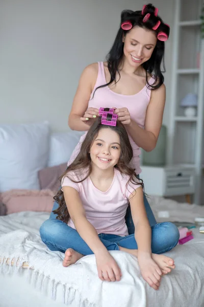 Jovem mãe com encrespadores de cabelo curling cabelo para sua filha — Fotografia de Stock