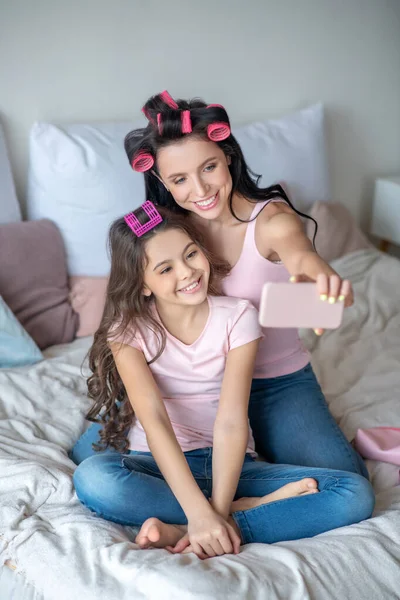 Mãe e filha com encrespadores de cabelo fazendo selfie — Fotografia de Stock
