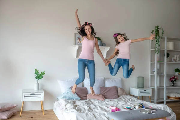 Mamma och dotter med hår papiljotter hoppar på sängen — Stockfoto