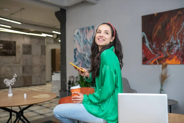 Joyful jovem mulher sentada na mesa perto de um laptop . — Fotografia de Stock