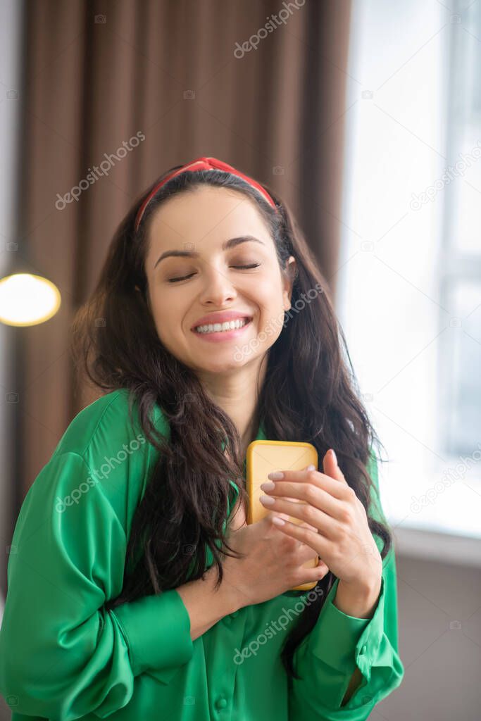 Happy woman clutching a smartphone closing her eyes.
