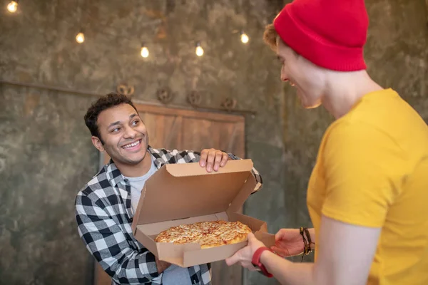 Hombre moreno con camisa a cuadros mostrando pizza a su amigo — Foto de Stock