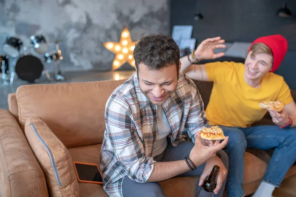 Dois jovens sentados no sofá e comendo pizza — Fotografia de Stock