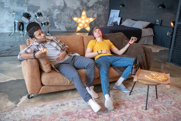 Två unga män sitter i soffan efter en trevlig middag — Stockfoto