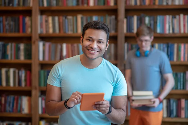 Dark-haired young latino in a blue tshirt holding a tablet — Stock Photo, Image