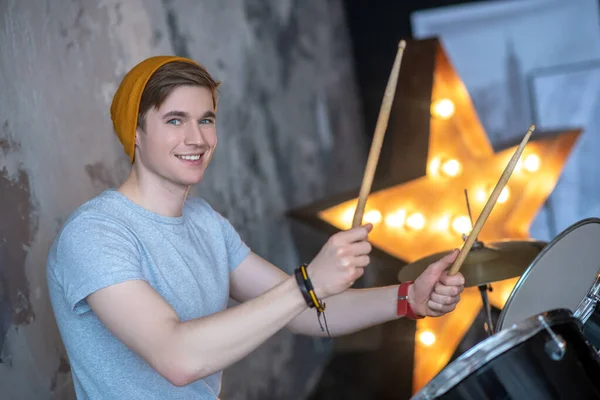 Młody człowiek w pomarańczowym kapeluszu uśmiecha się ładnie grając na perkusji — Zdjęcie stockowe