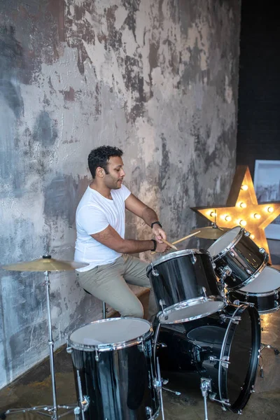 Donkerharige jonge latino in een wit tshirt zittend aan de drums — Stockfoto