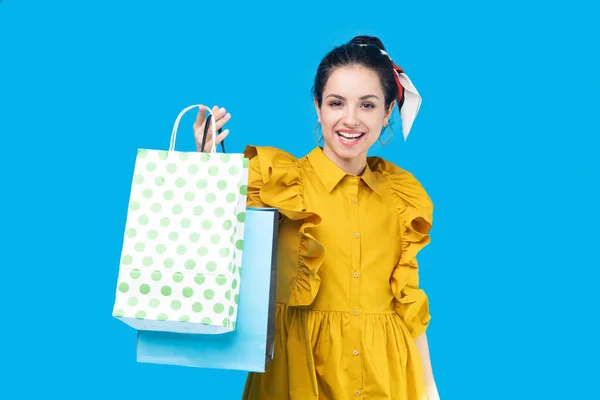 Młoda kobieta w musztardowej sukience pokazuje torbę na zakupy — Zdjęcie stockowe