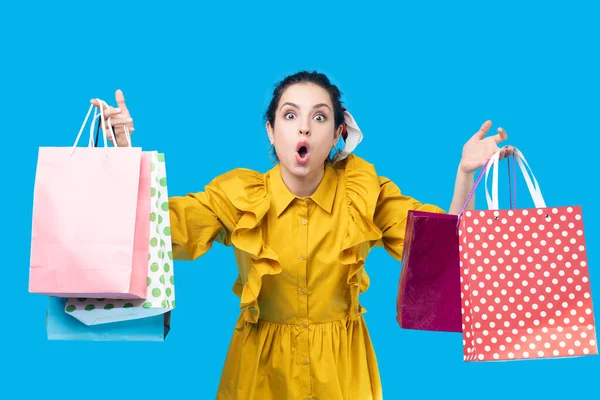 Mujer joven en un vestido de mostaza sosteniendo bolsas de compras y mirando sorprendido — Foto de Stock