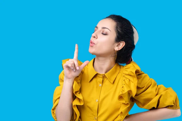 Junge Frau im Senfkleid pustet in Fingergewehr — Stockfoto