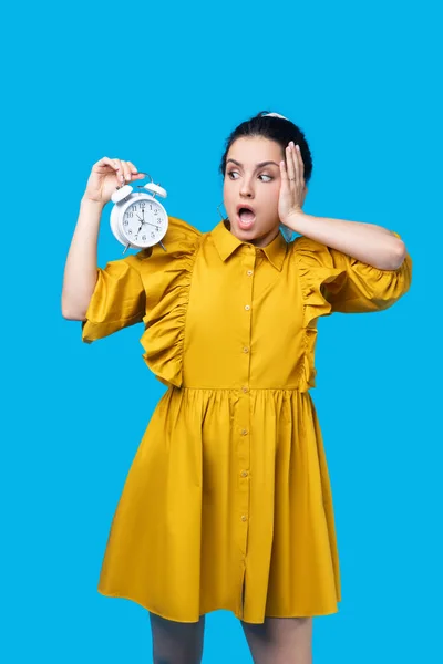 Žena v hořčičných šatech drží hodiny a vypadá vystresovaně — Stock fotografie