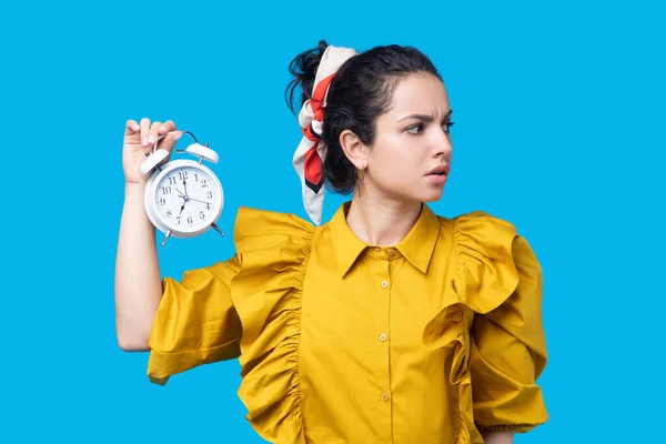 Vrouw in een mosterdjurk die een klok vasthoudt en zich zorgen maakt — Stockfoto