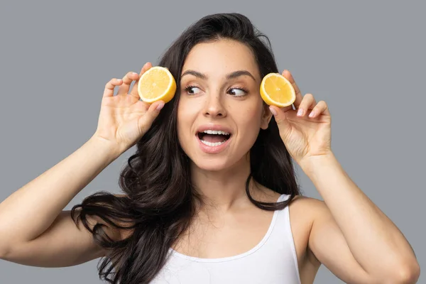 Beautiful dark-haired girl holding an orange in her hands and looking surprised — Stock Photo, Image