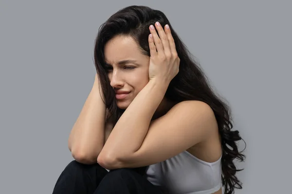 Mooi donkerharig meisje in een witte top houdt haar hoofd vast en voelt zich gestrest — Stockfoto