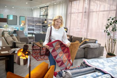 Mağazada elinde halıyla bekleyen bir kadın..