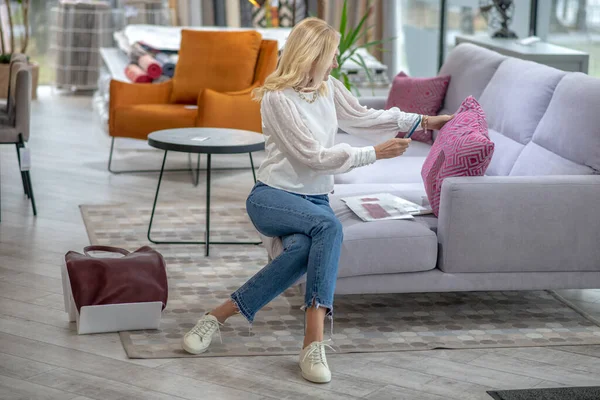 Donna seduta su un divano a fotografare un cuscino rosa . — Foto Stock