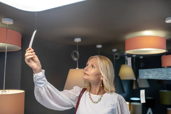 Mujer con collar mirando el precio de una lámpara de araña . —  Fotos de Stock