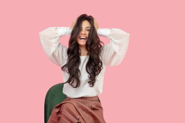 Beyaz bluzlu güzel esmer kadın ellerini başının altına koyuyor.